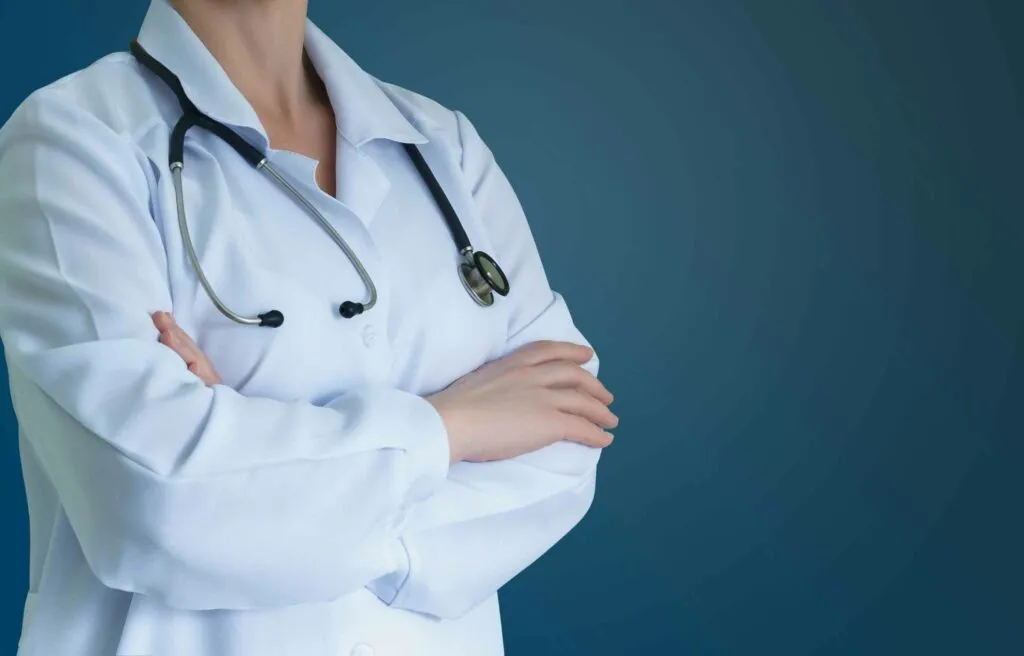 Doctor standing with arms crossed, wearing a white lab coat and stethoscope, representing relocation for physicians in professional healthcare roles.