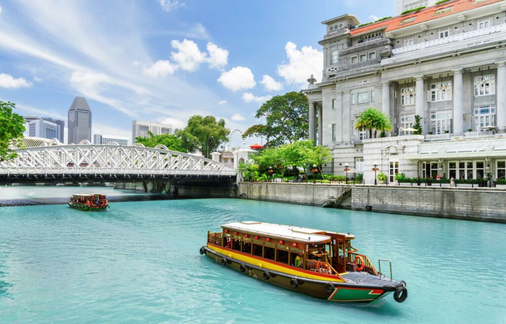 Scenic view of a boat cruising along the Singapore River with a historic bridge and colonial architecture in the background.