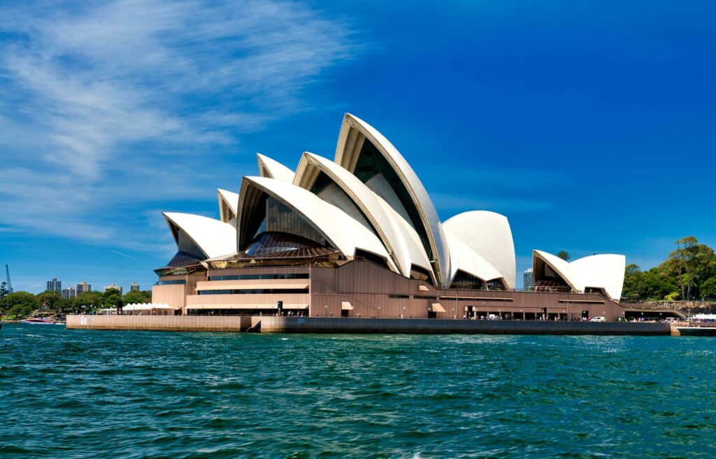 Sydney Opera House in Australia viewed from the harbor under a clear blue sky.