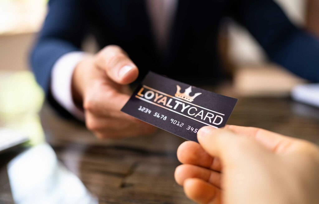 Person handing over a black loyalty card with crown logo and numbers printed on it.