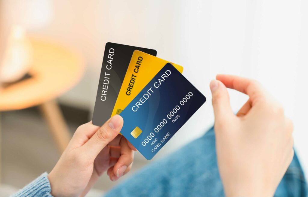 Hands holding three different credit cards in black, yellow, and blue colors.