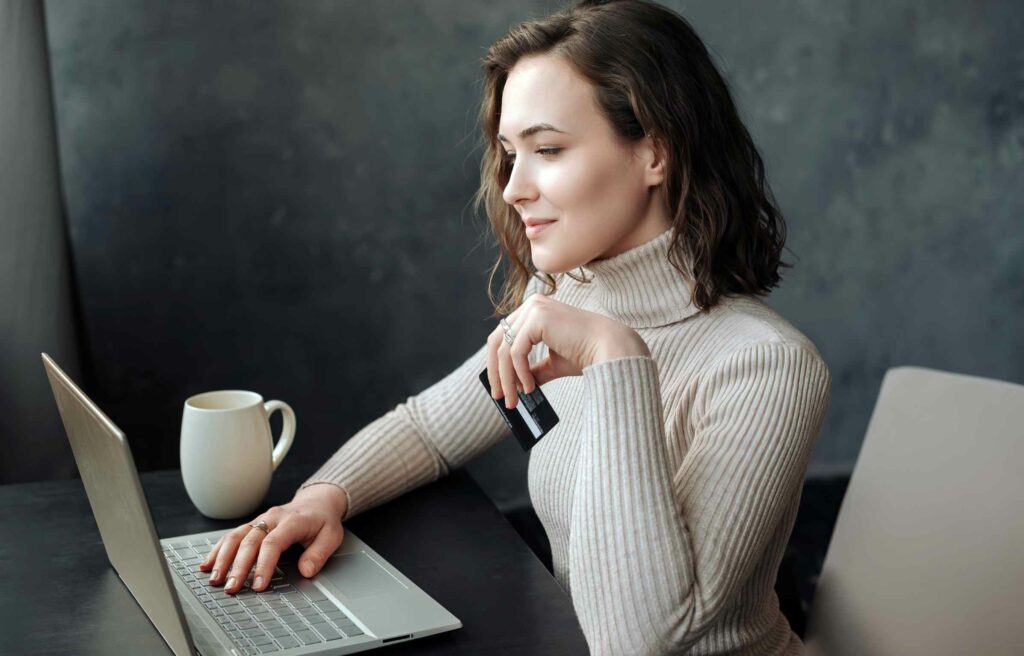 A woman holding a credit card while browsing on her laptop, researching how much are Chase Ink points worth and planning her next redemption.