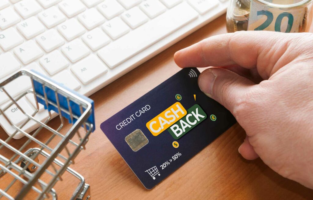 Hand holding a cashback credit card near a keyboard and shopping cart, symbolizing rewards and the value of Chase Ink points.