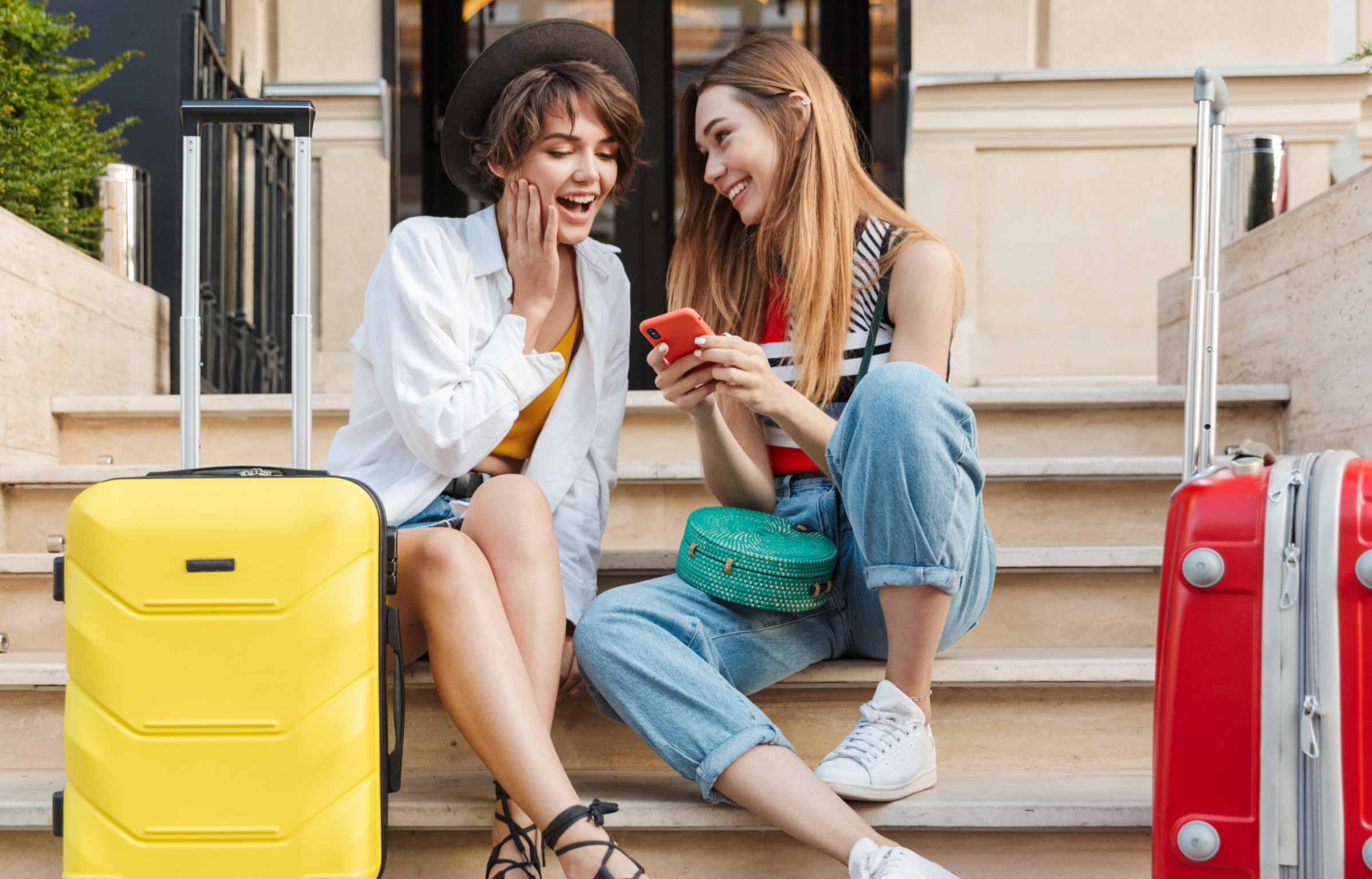 Happy Two Girls With Luggage Using Phone