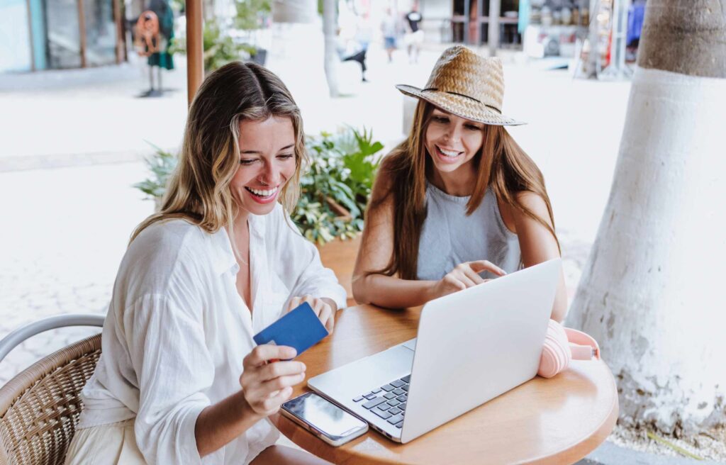 Two Women at Outdoor Cafe with Laptop and Credit Card Selecting the Best Credit Cards with No Annual Fee and Cash Back