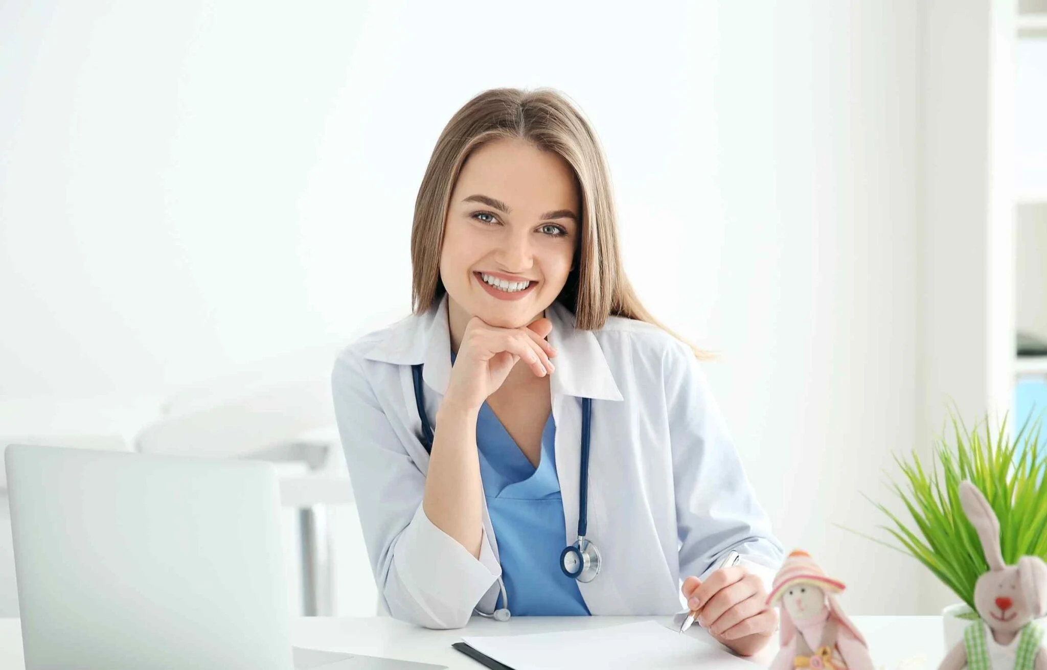 Smiling female doctor writing notes at a clinic desk with stethoscope