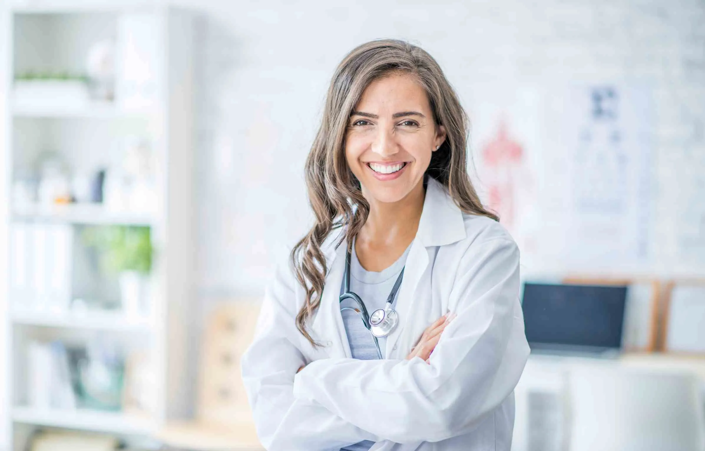 Confident female doctor standing with arms crossed in bright clinic
