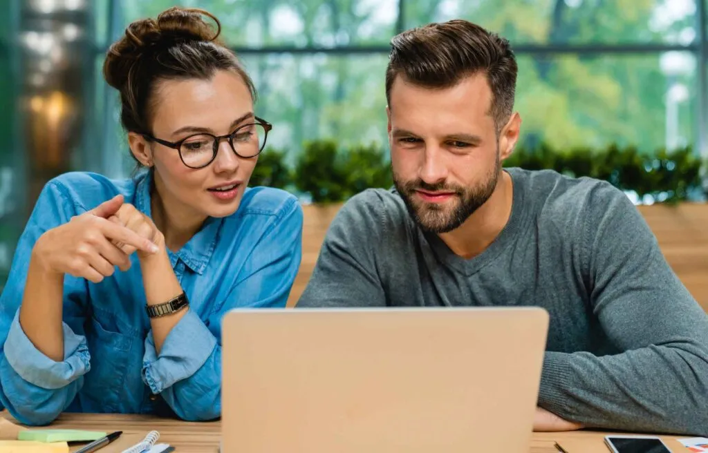 Two colleagues collaborating while looking at a laptop in a bright workspace.