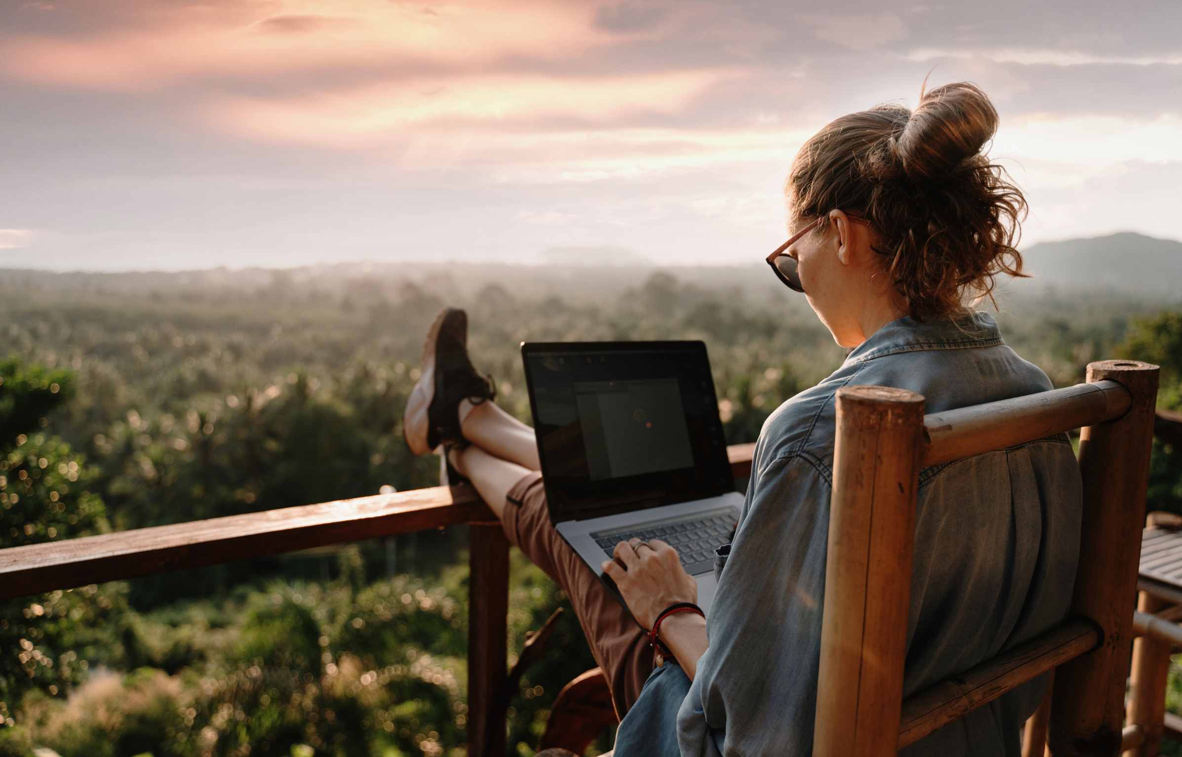 Young girl downshifter working at a laptop at sunset or sunrise on the top of the mountain to the sea, working day.