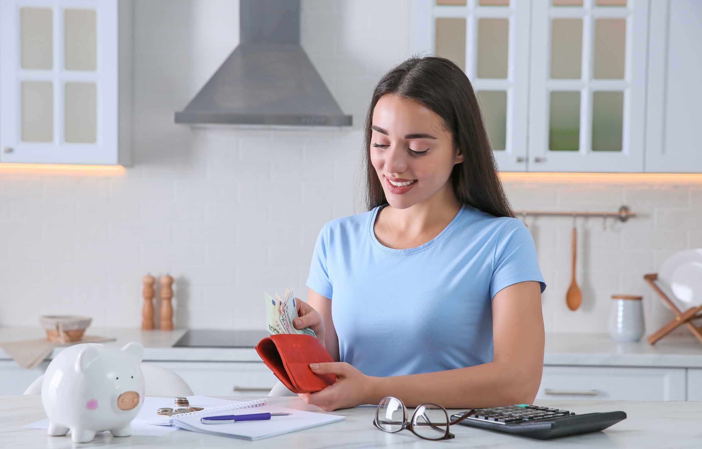 Young woman counting money at table in kitchen