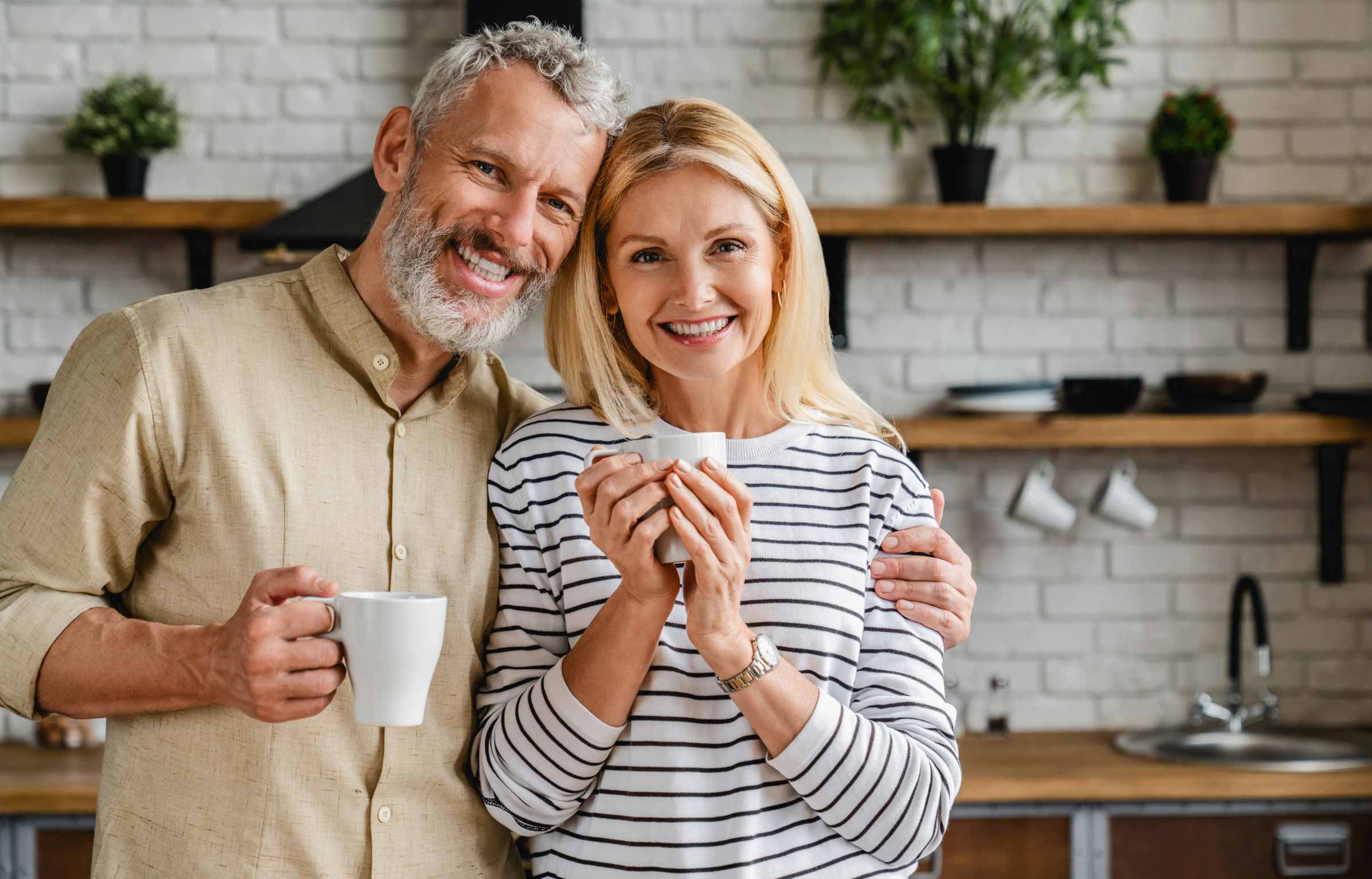 Beautiful middle aged couple drinking tea or coffee at home while looking at camera