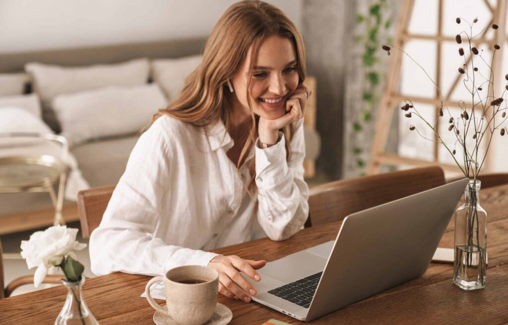 Cheerful cute beautiful business woman sit indoors in office using laptop computer listening music with earphones and corporate relocation in 2025