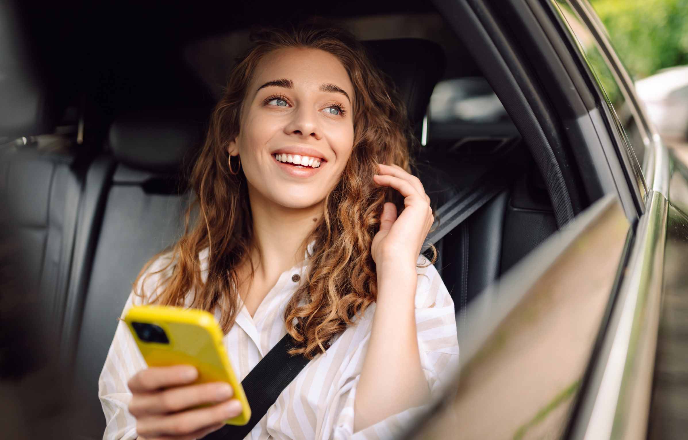 Beautiful young woman uses a smartphone while sitting in the back seat of a car. Concept of technology, traveling by car, business.