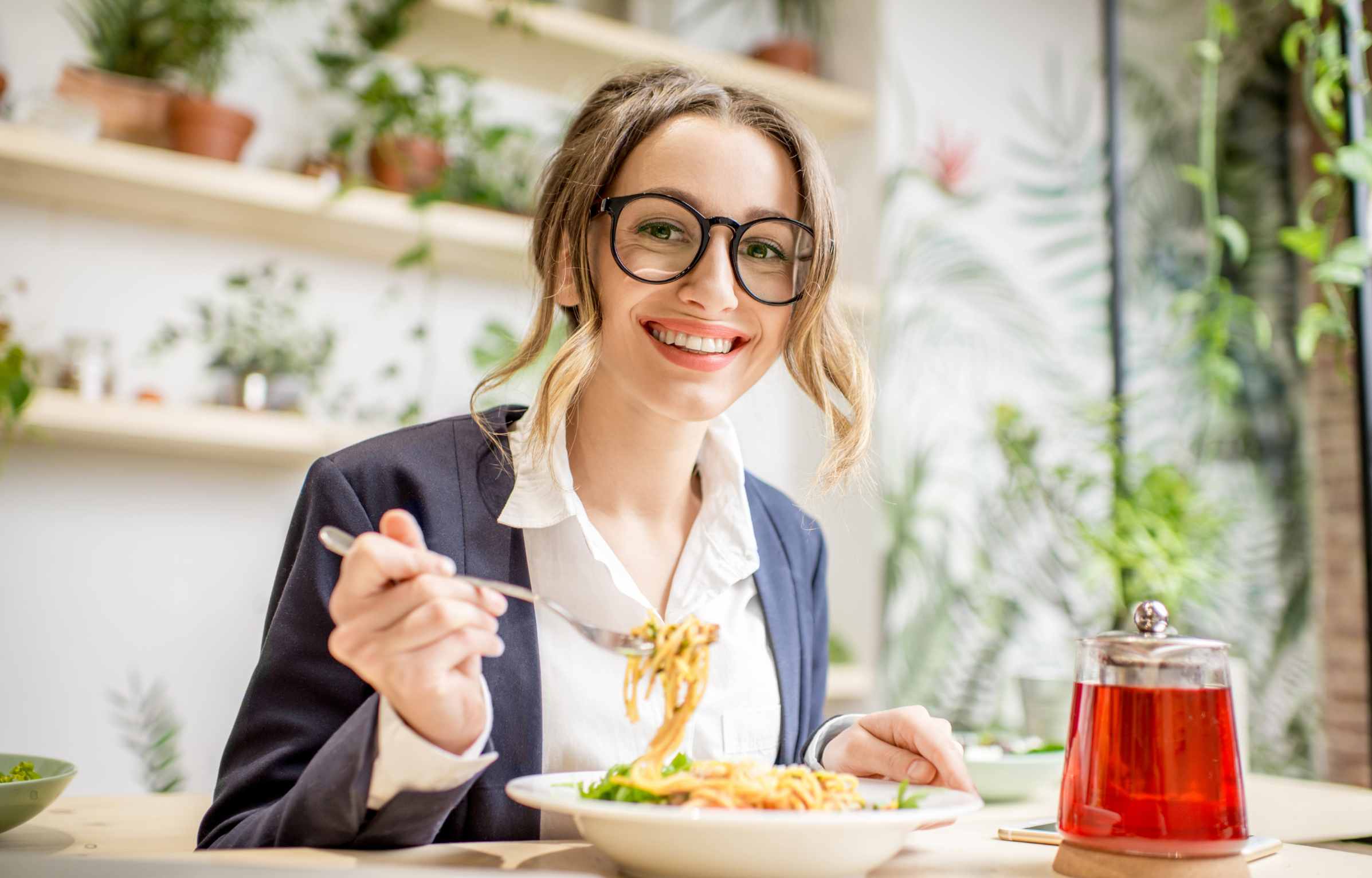 Businesswoman having lunch with pasta and fruit tea at the vegan restaurant on the green background