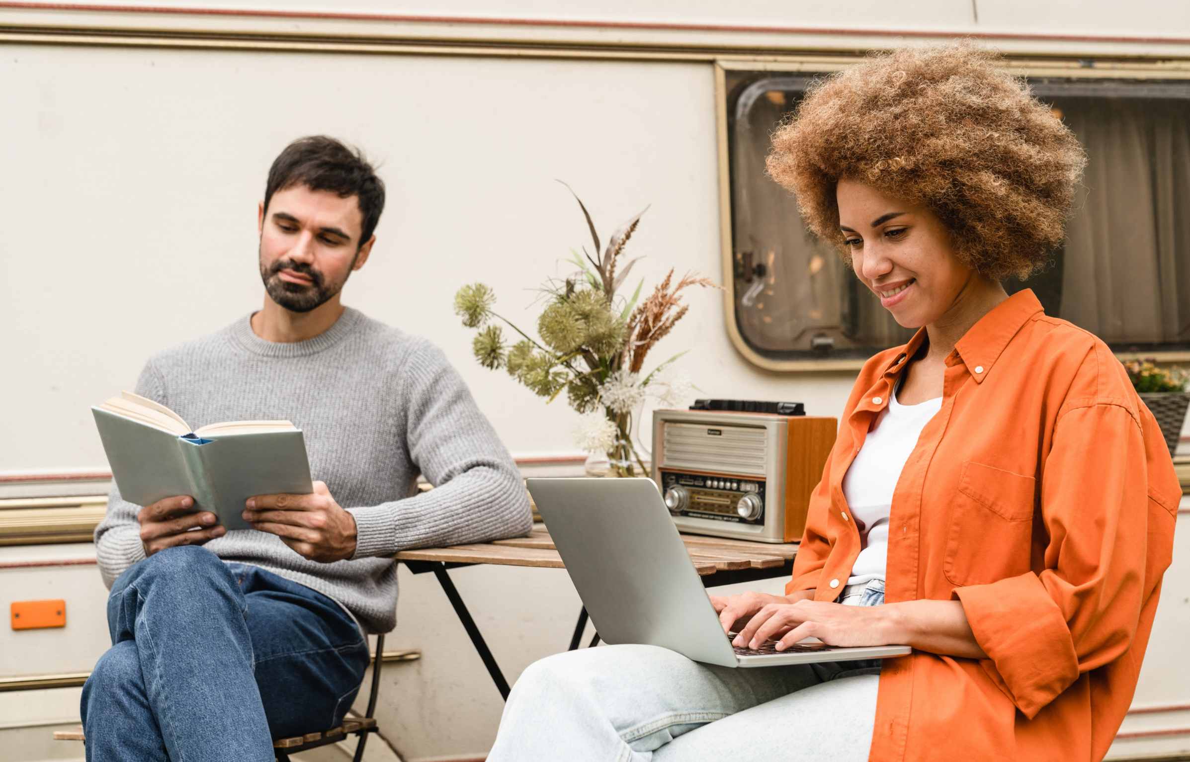 Mixed-race couple spouses boyfriend and girlfriend husband and wife using laptop and reading book, working studying remotely while traveling by van motor wheel camper home trailer