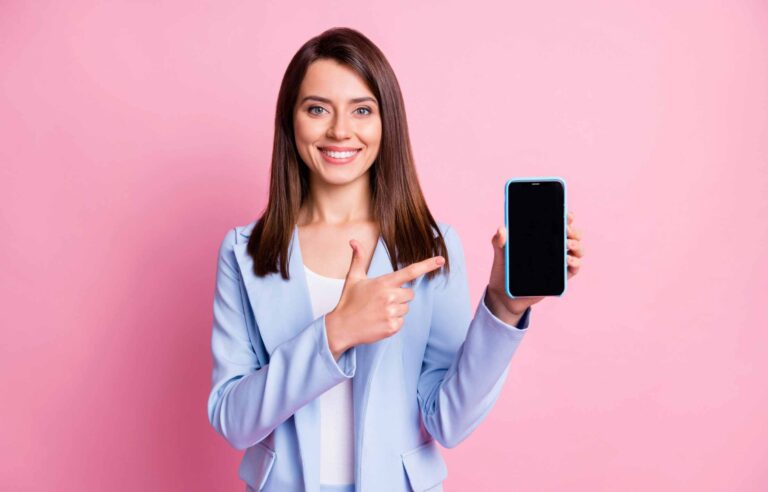 Photo of young beautiful girl happy smile point finger cellphone advert promo advice recommend isolated over pink color background