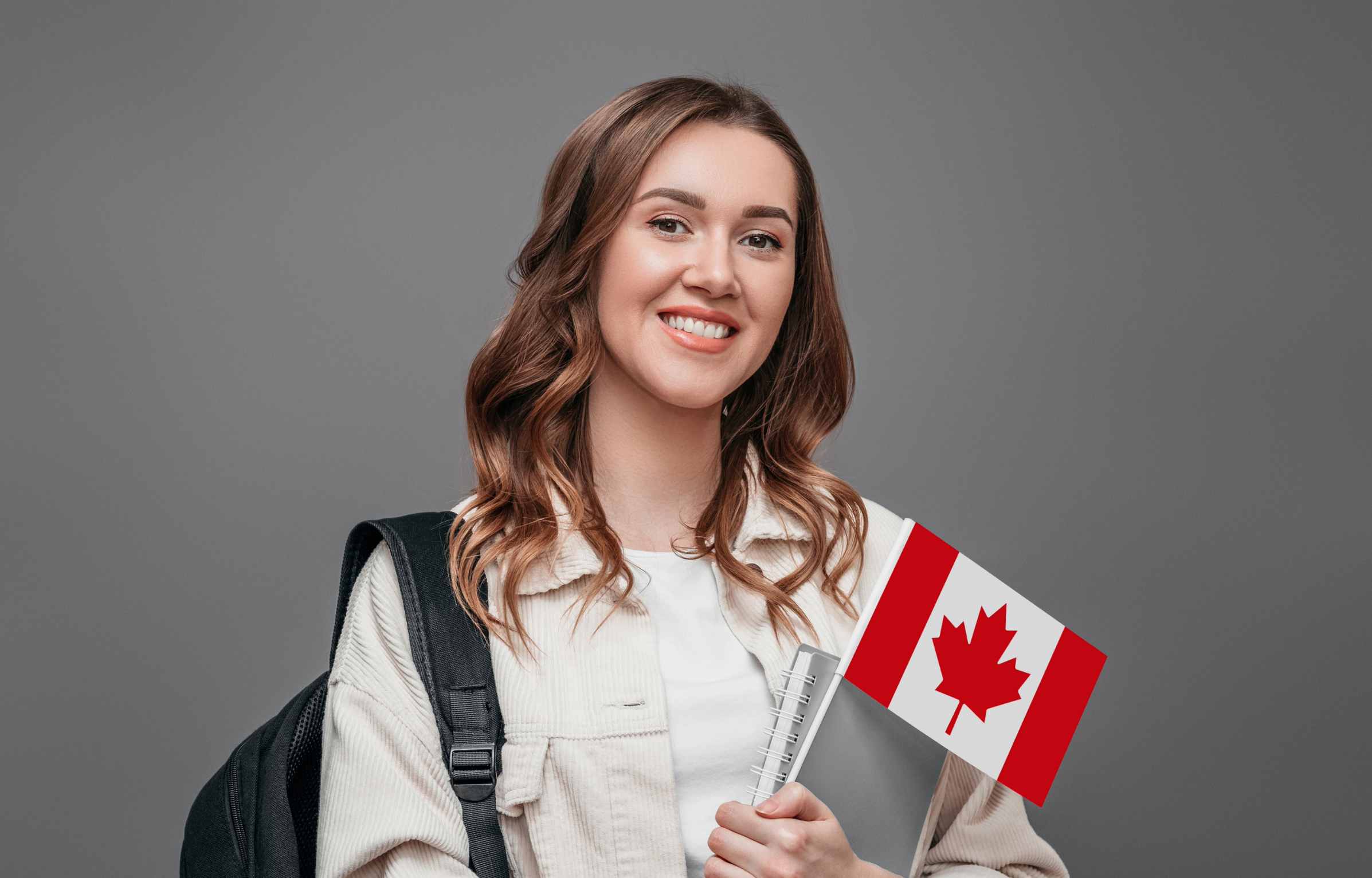 Young girl student smiling and holding a small canada flag isolated on dark gray background, Canada day, holiday, confederation anniversary, copy space