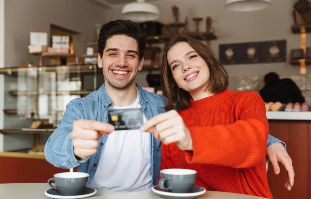 Cheerful young couple sitting at the cafe table and showing plastic credit card