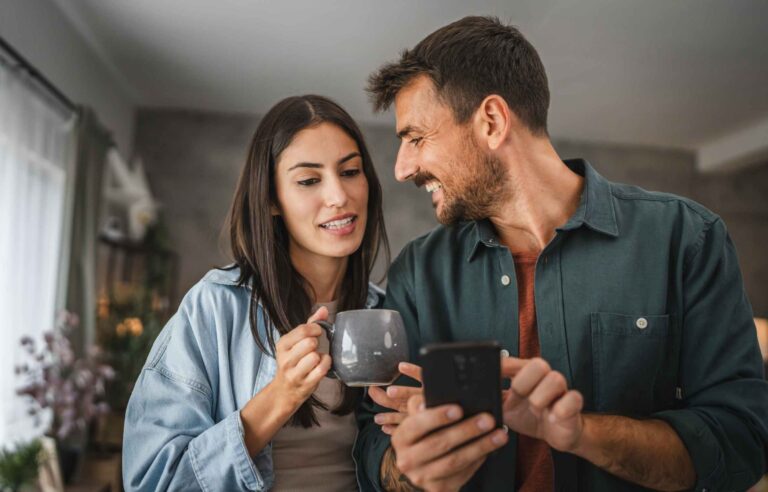 Couple in love resting on comfy couch having fun using smart phone apps