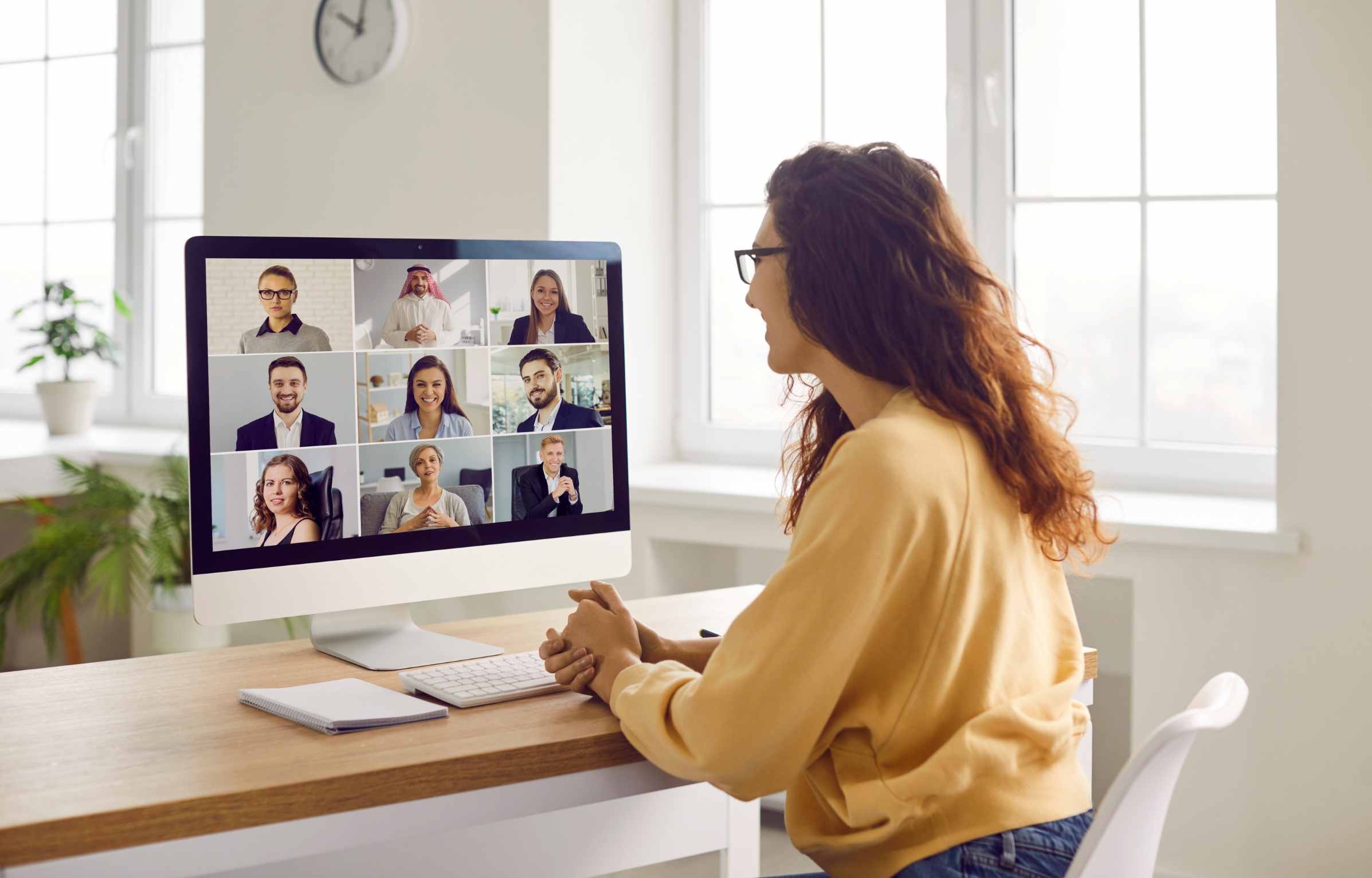 Corporate business team having a remote meeting. Young woman in casual clothes sitting at her desk at home, attending an online conference, looking at the computer screen, and smiling