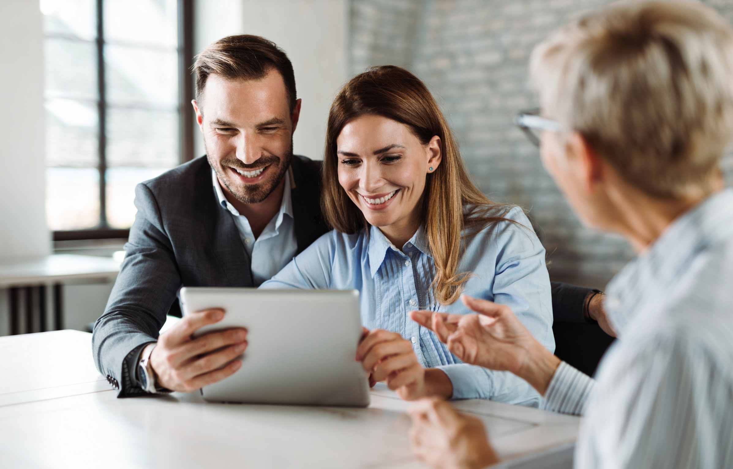 Happy couple using digital tablet while having a meeting with their insurance agent in the office