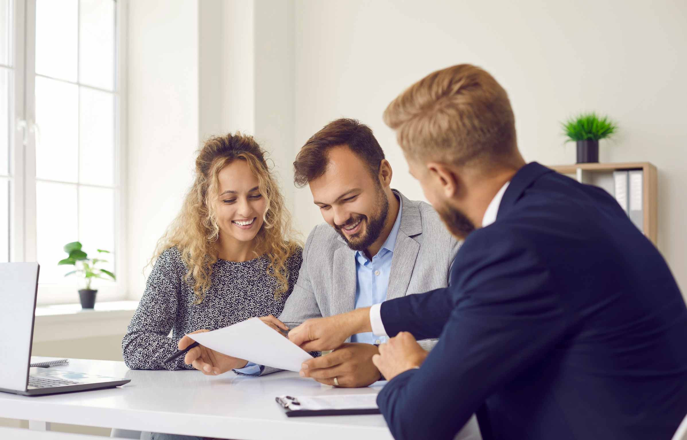 Happy young family at meeting in office signs document on purchase of real estate or loan agreement. Head of bank, realtor or financial advisor submits contract and indicates place of its signing