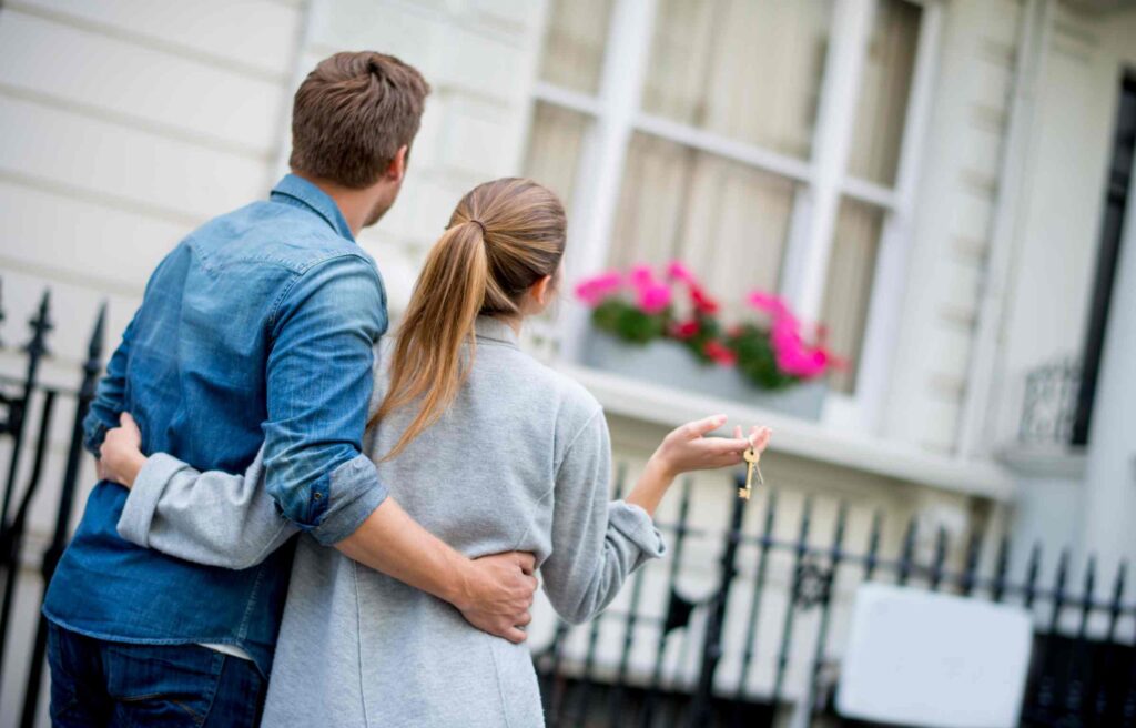A couple holding a new house key, looking at their new home after using relocation services for individuals.