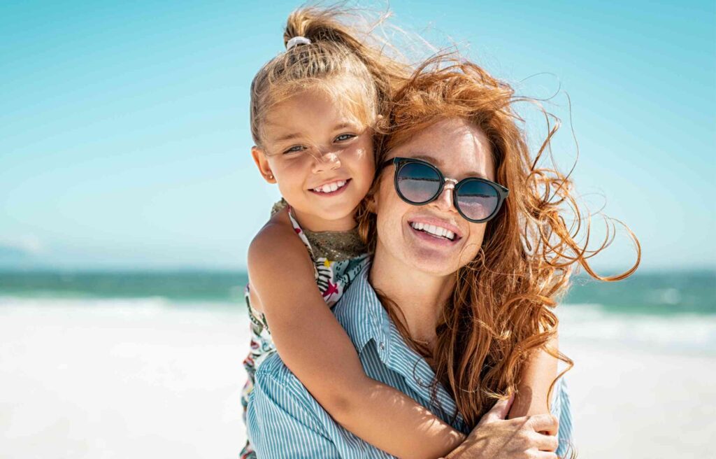 A happy mother and daughter enjoy a sunny day at the beach, smiling together.