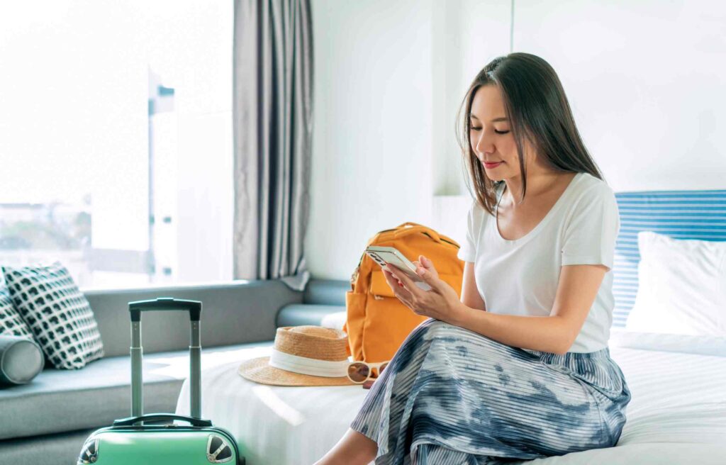  A woman in a hotel room checking her phone, likely comparing ihg vs. hilton.