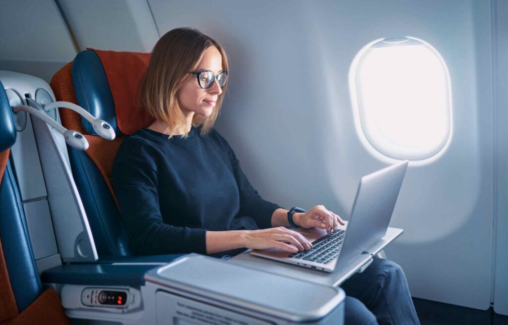 Pretty young businesswoman working on a laptop while sitting in airplane with the delta business traveler program