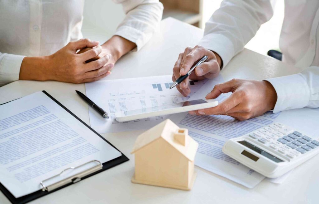 Two people are reviewing documents and discussing a relocation mortgage with a miniature house model on the table.