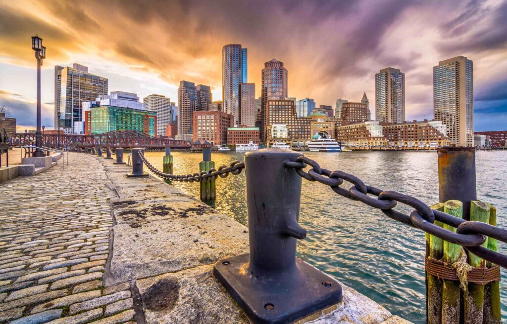 Downtown Boston skyline at sunset with boardwalk and boats, reflecting why many ask, is boston a good city to live and work.