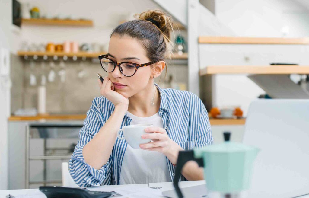 A woman with glasses sits at a table. She appears to be thinking about costs related to relocation services for individuals.