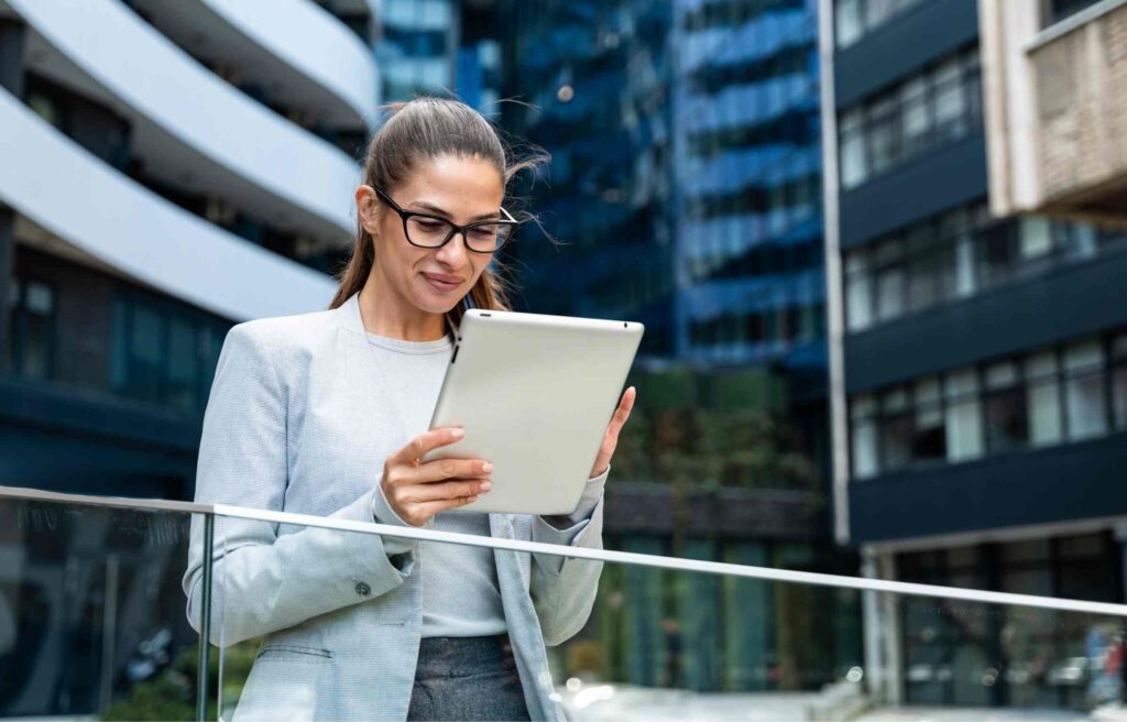 A businesswoman standing outside an office building using a tablet, researching how to move a business to another state.