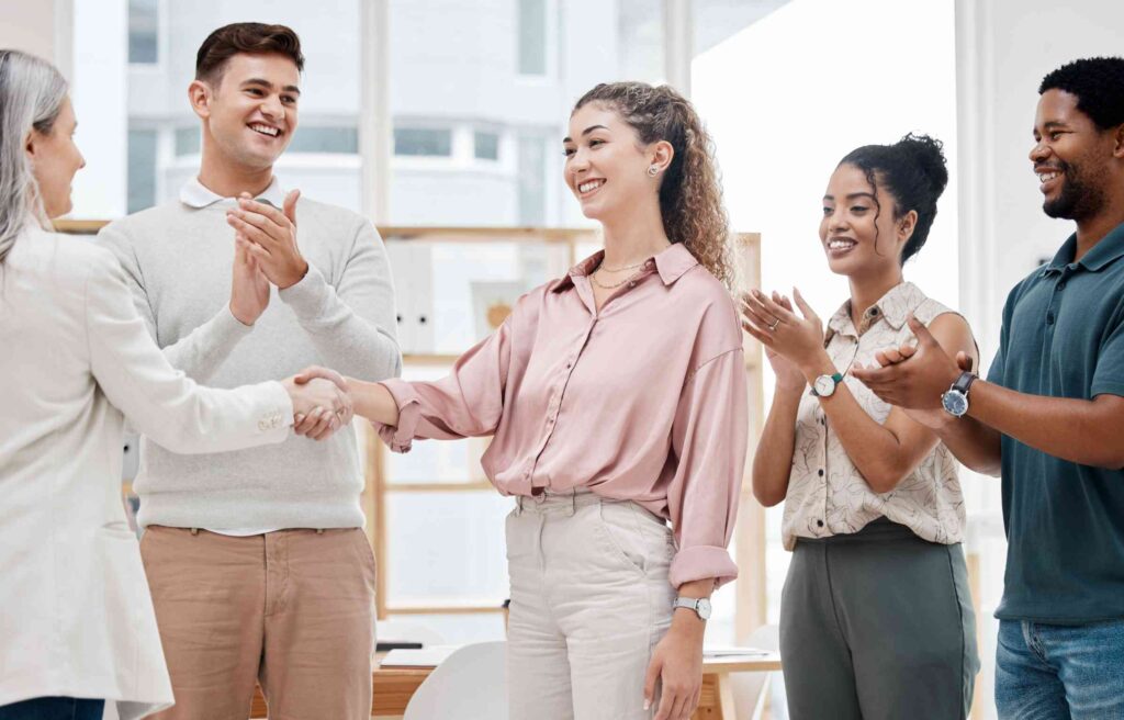 A woman shakes hands in her new office as colleagues applaud, showing a smooth move with job relocation services.