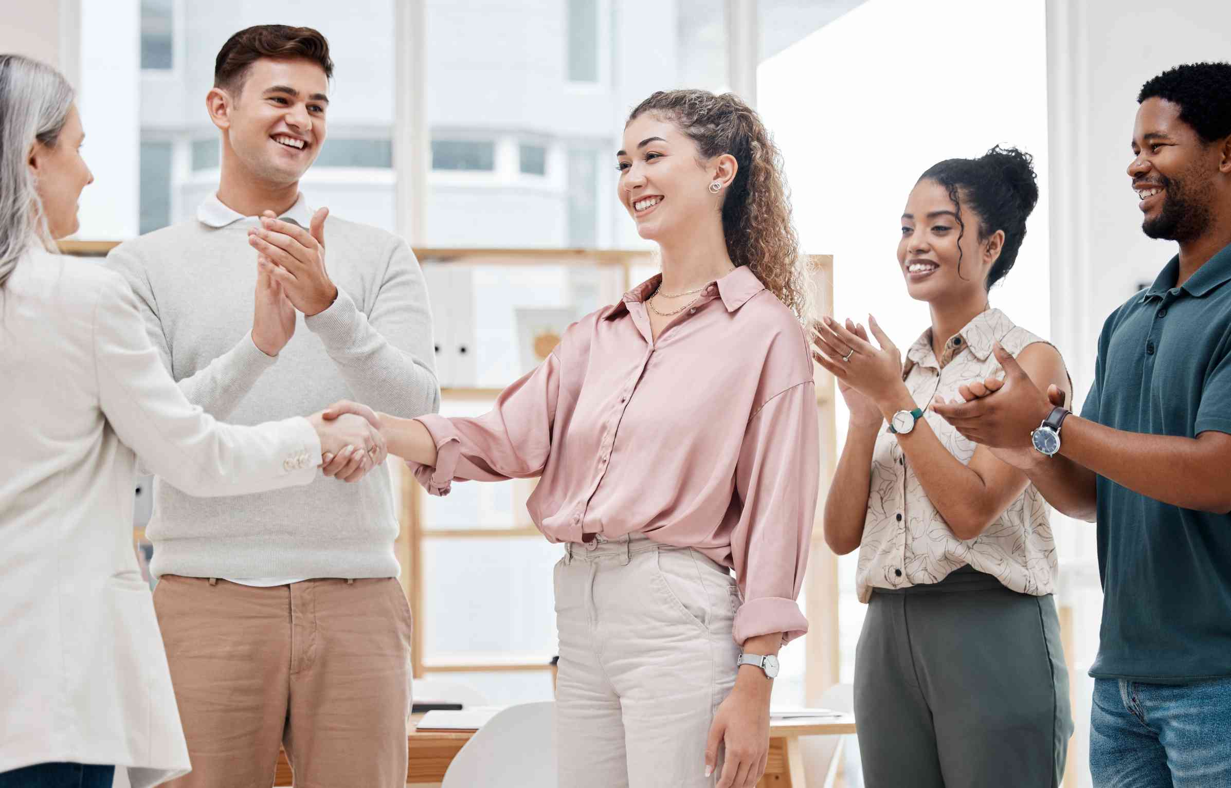 A woman shakes hands in her new office as colleagues applaud, showing a smooth move with job relocation services.