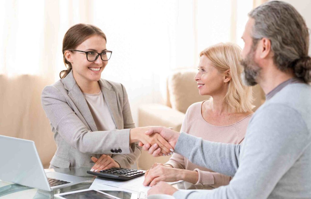 A young retirement relocation consultant shakes hands with a retiree couple during a consultation meeting.