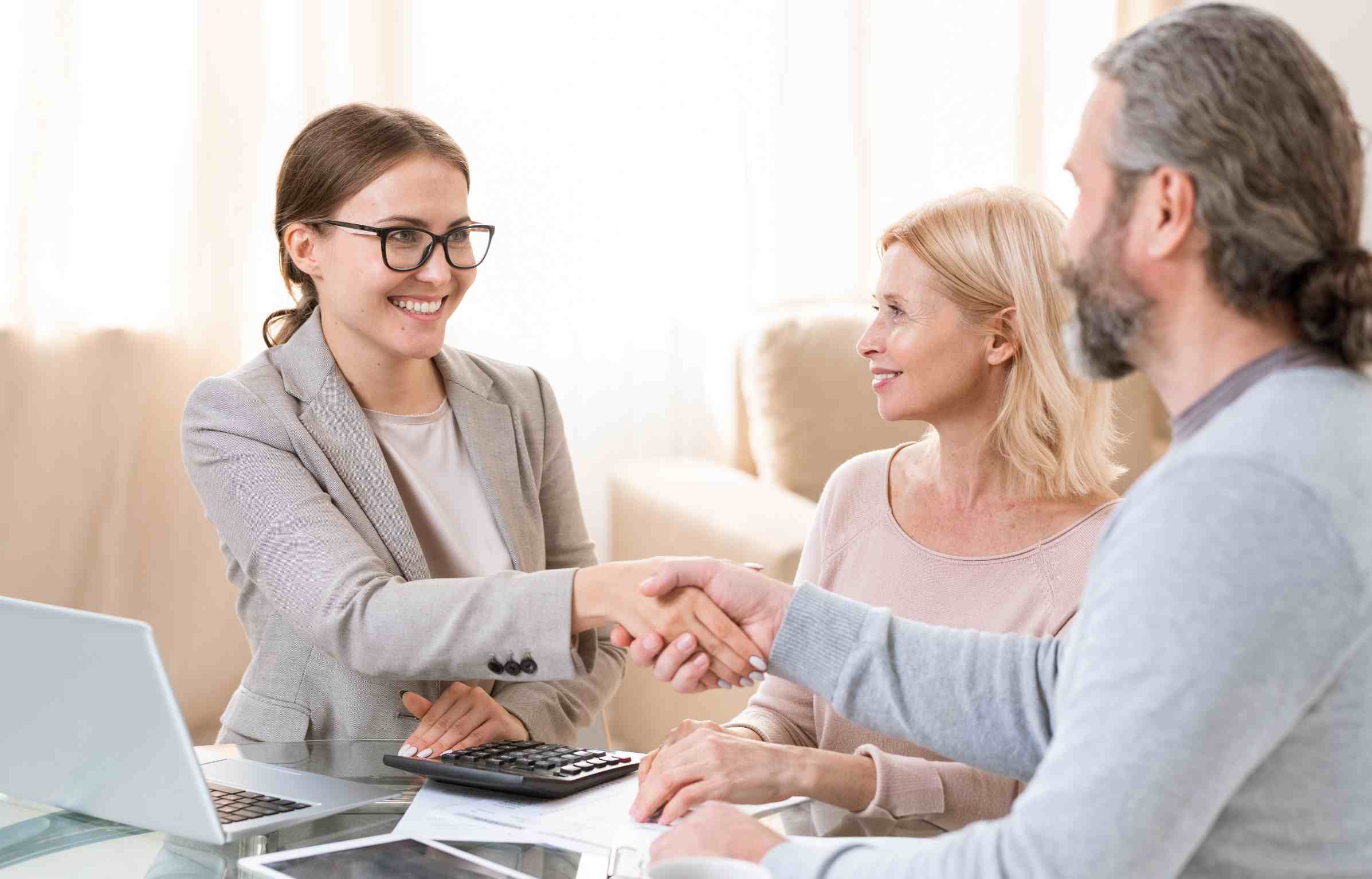 A young retirement relocation consultant shakes hands with a retiree couple during a consultation meeting.