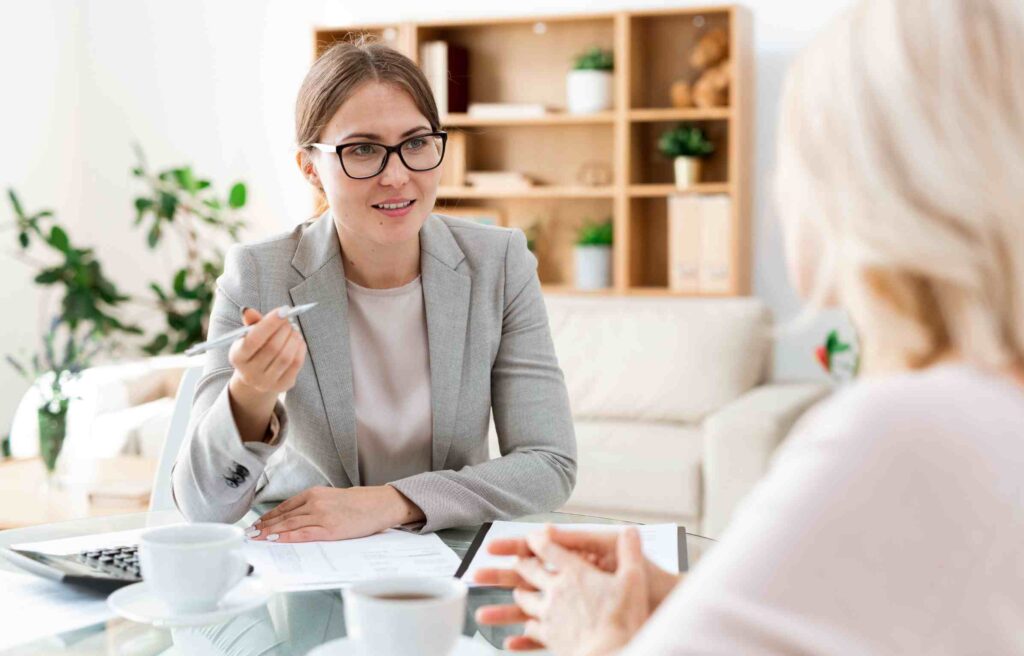 A young retirement relocation consultant discusses moving plans with a retiree in a bright, homey setting.