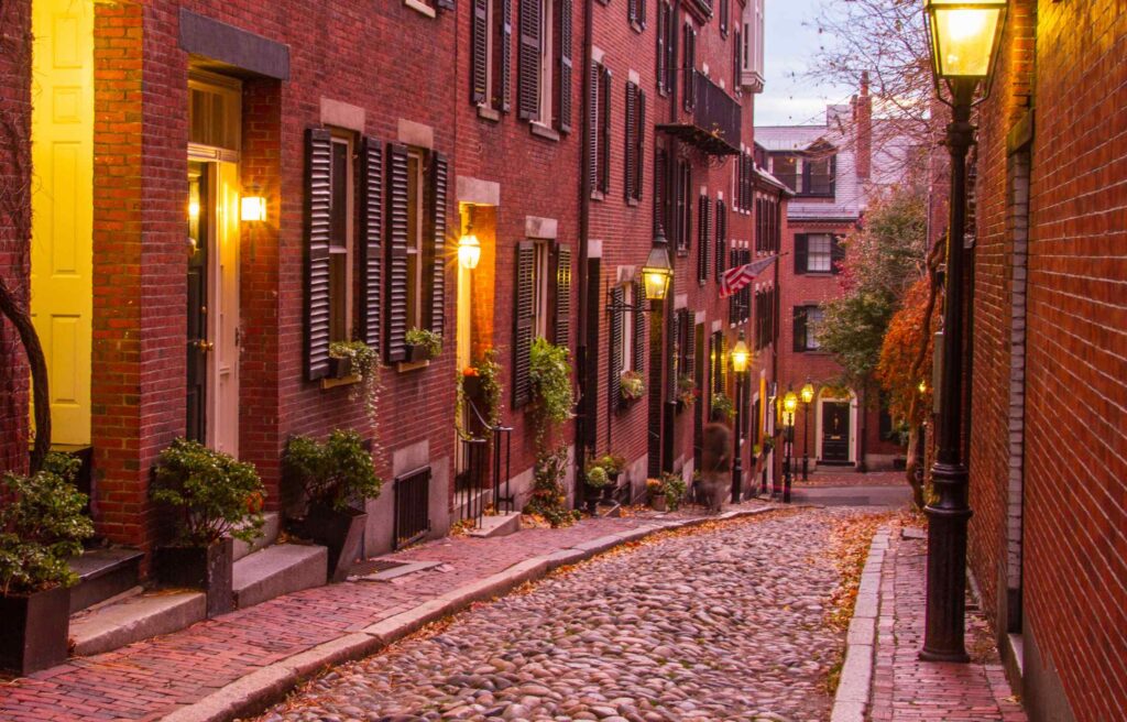 Cobblestone street lined with historic red brick townhouses and glowing street lamps in Beacon Hill.