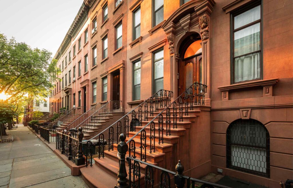 Tree-lined street with historic brownstone homes in Brookline at sunset.