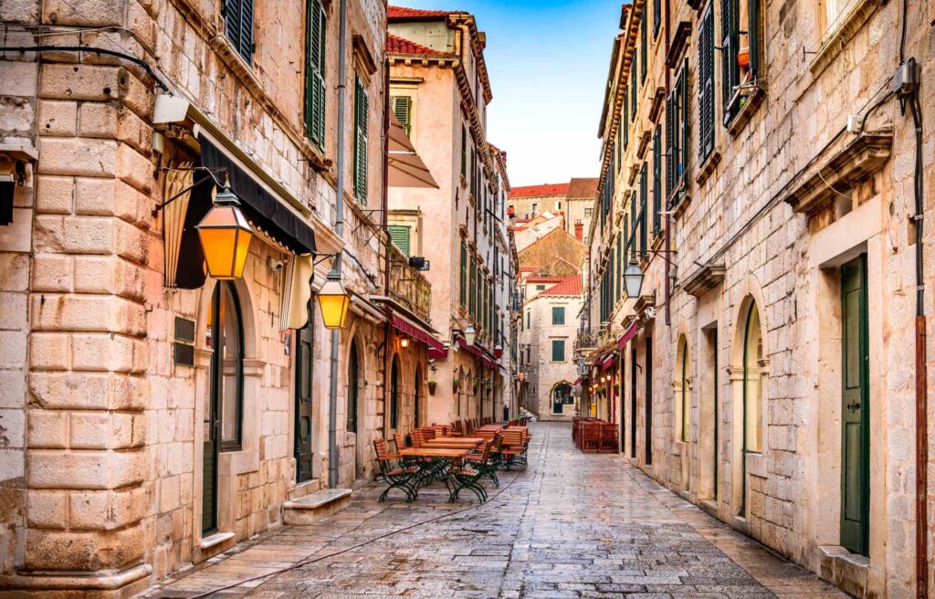 Narrow stone street in Croatia lined with historic buildings, outdoor cafes, and warm street lamps.