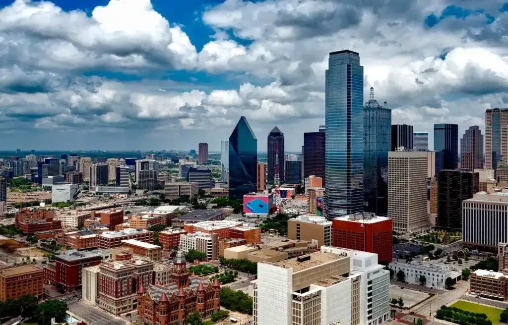 Dallas Texas city skyline with modern high-rise buildings under a partly cloudy sky.
