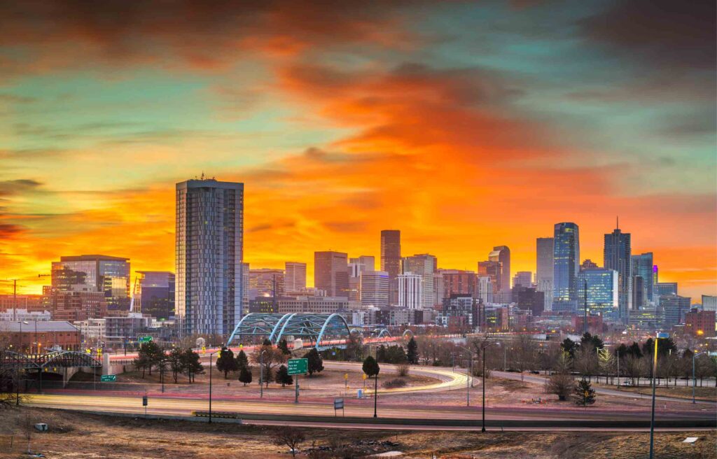 Denver, Colorado skyline at sunset with glowing orange sky and city lights reflecting the vibrant downtown.