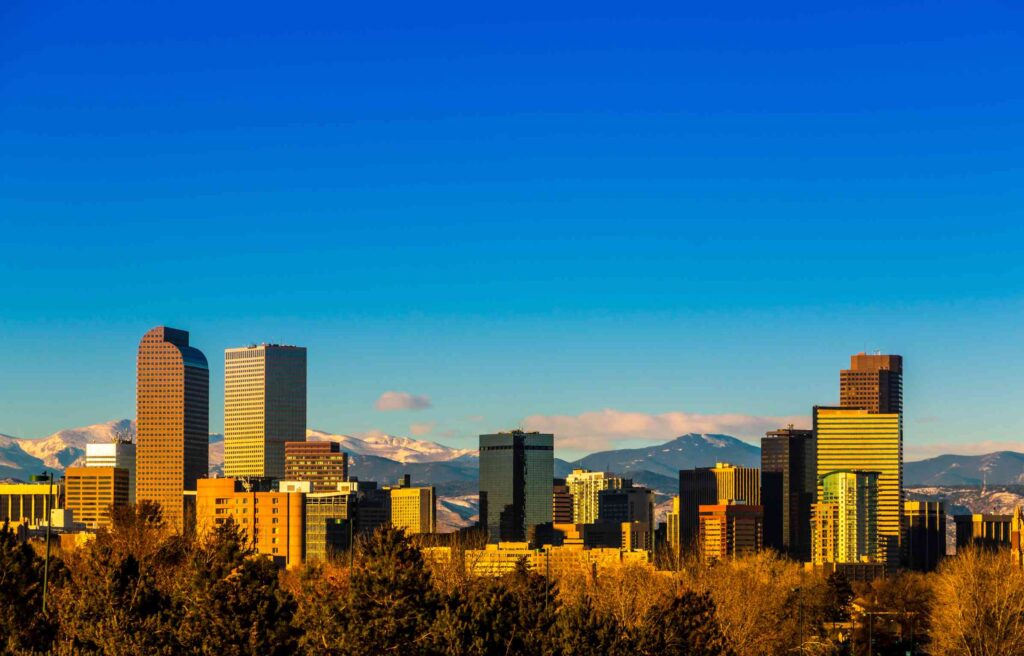 Denver skyline with modern high-rise buildings and the Rocky Mountains in the background on a clear day.