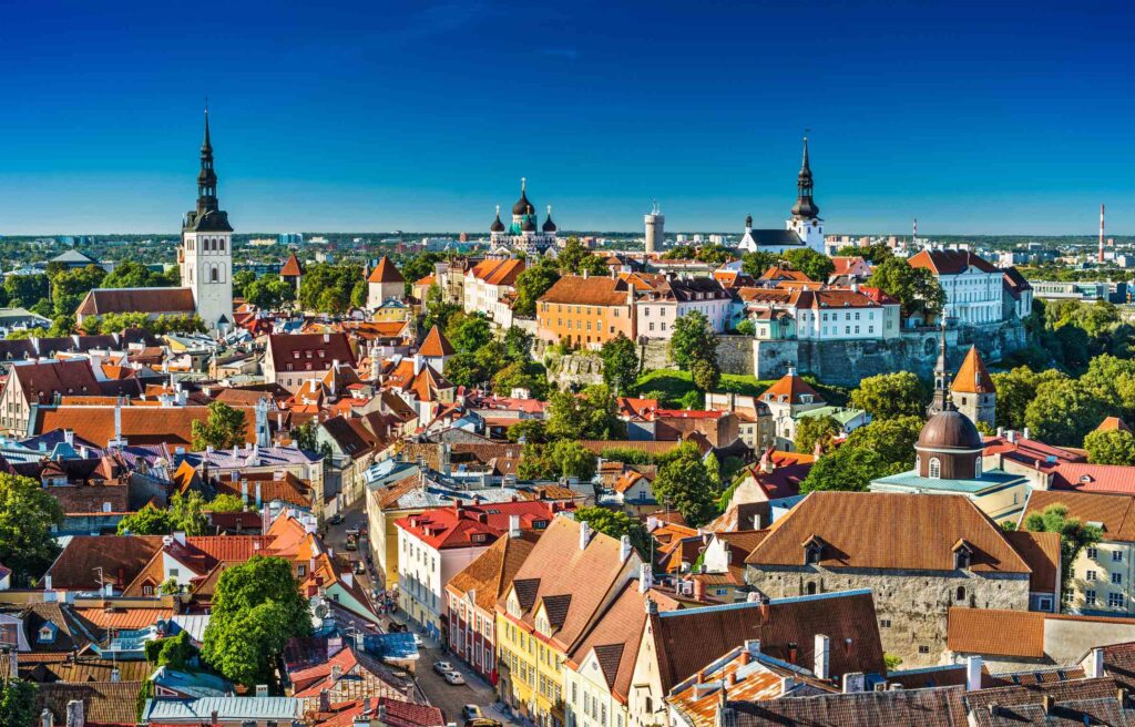 Aerial view of historic city in Estonia with colorful buildings, red-tiled roofs, and church spires under a clear blue sky.