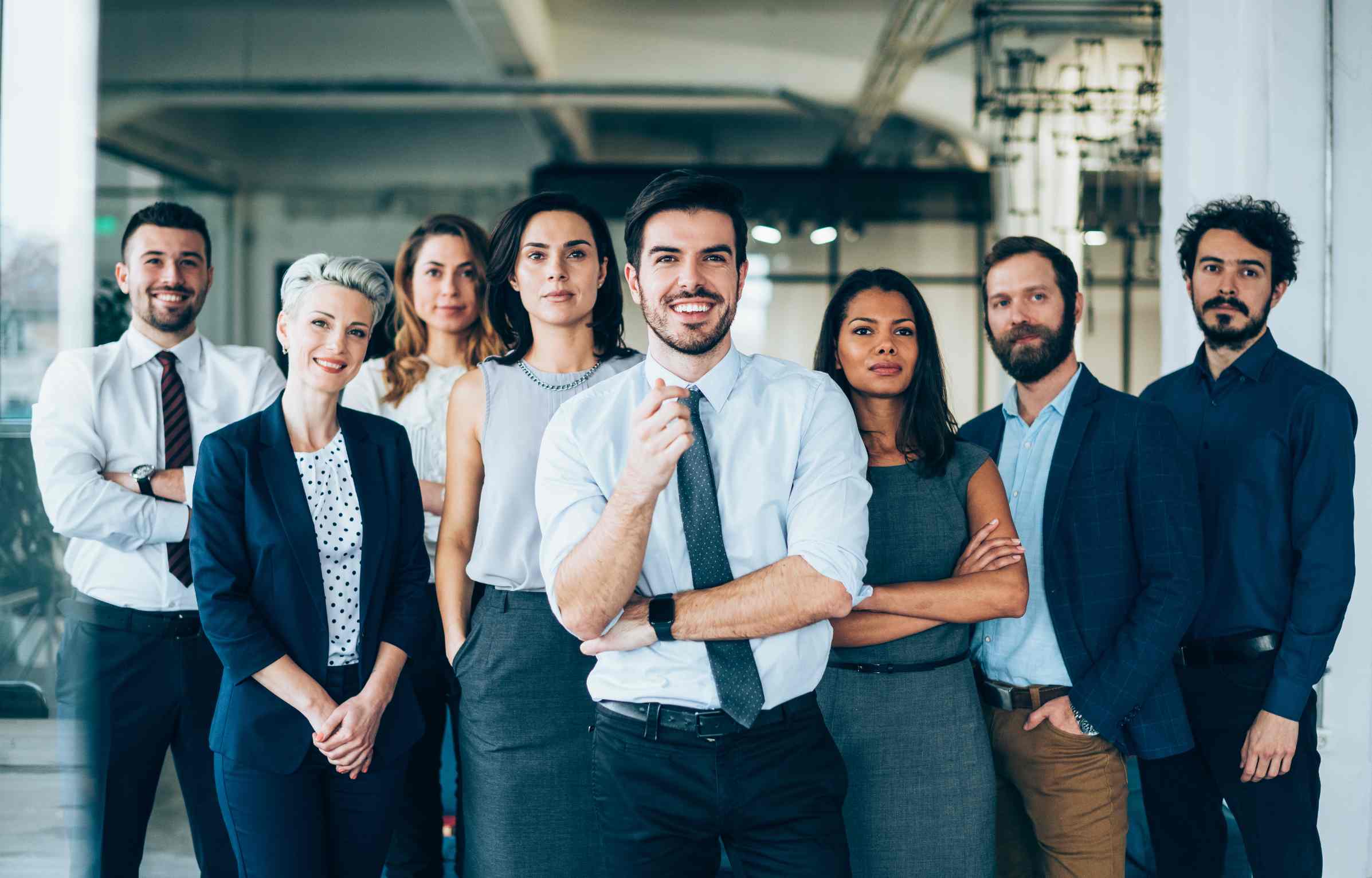 Group of confident IT professionals standing together in an office, dressed in business attire, representing a diverse technology team.