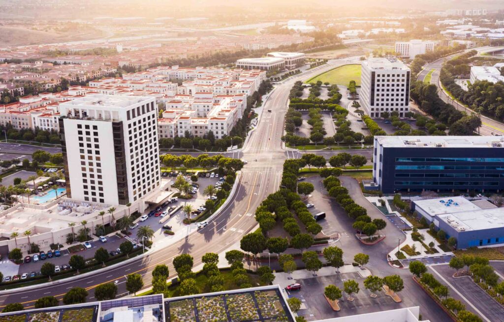 Aerial view of Irvine, California showing modern office buildings, residential areas, and tree-lined streets at sunset.