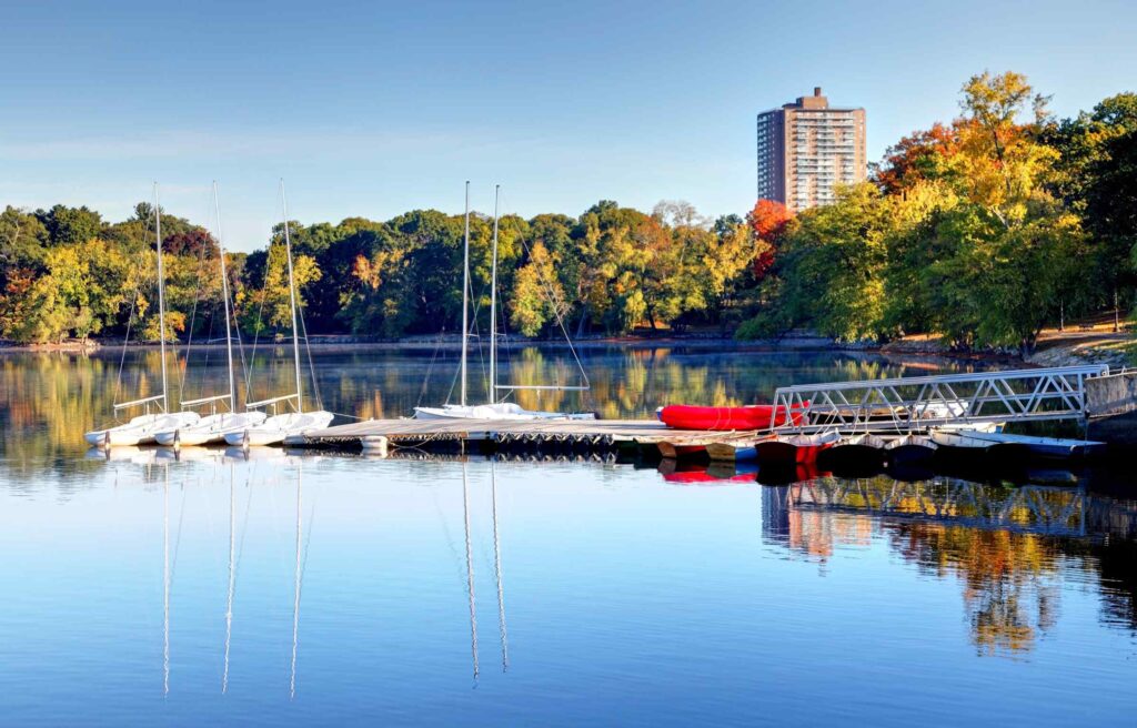 Sailboats docked on Jamaica Pond surrounded by colorful trees in Jamaica Plain, Boston.
