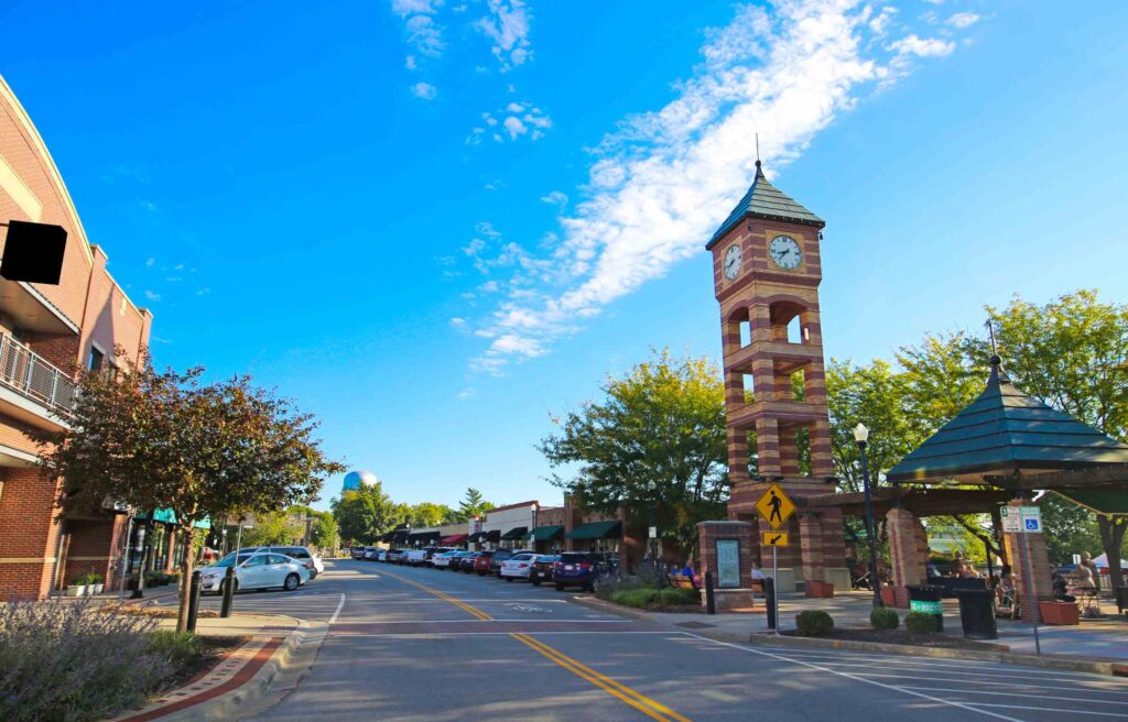 Downtown Overland Park, Kansas with a clock tower, local shops, and cars parked along the street on a bright sunny day.